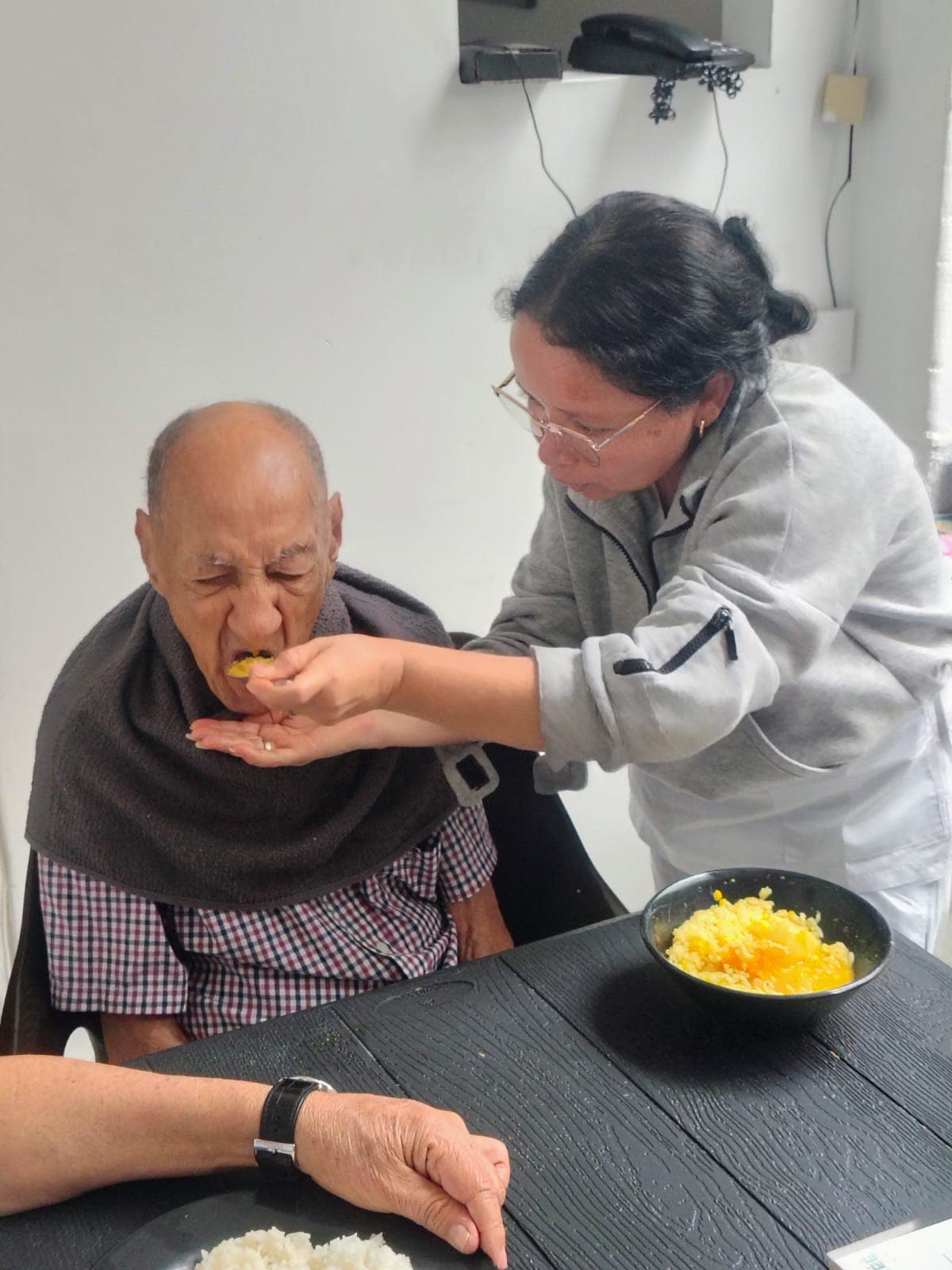 Una auxiliar ayudando a comer a un residente